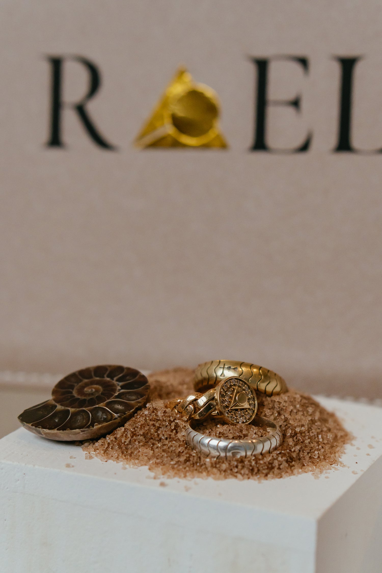 2 18k Gold rings and a .925 sterling silver ring sit atop a white mixed with sand. 